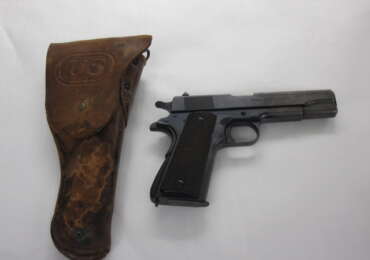 An original U.S. M1911 pistol shown beside its period leather flap holster
