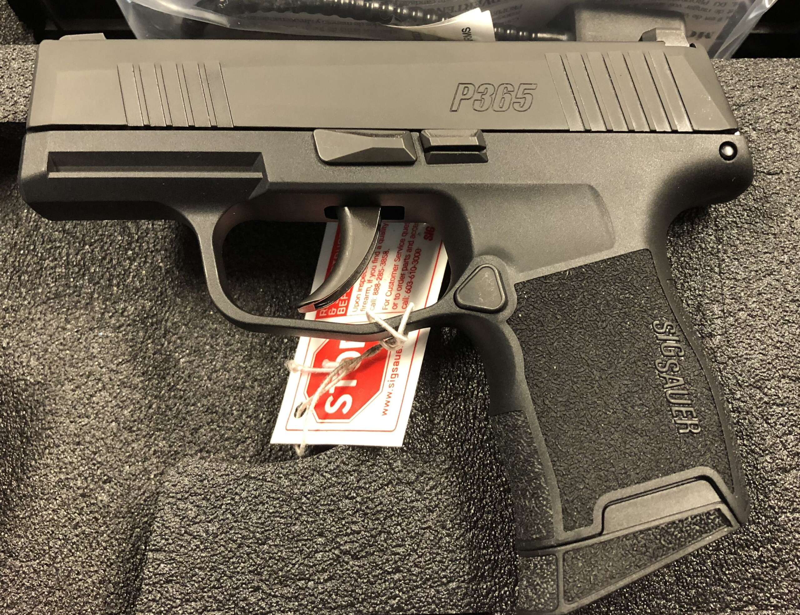 The left side of a new-in-box SIG Sauer P365 showing its slide markings, takedown lever and grip texture